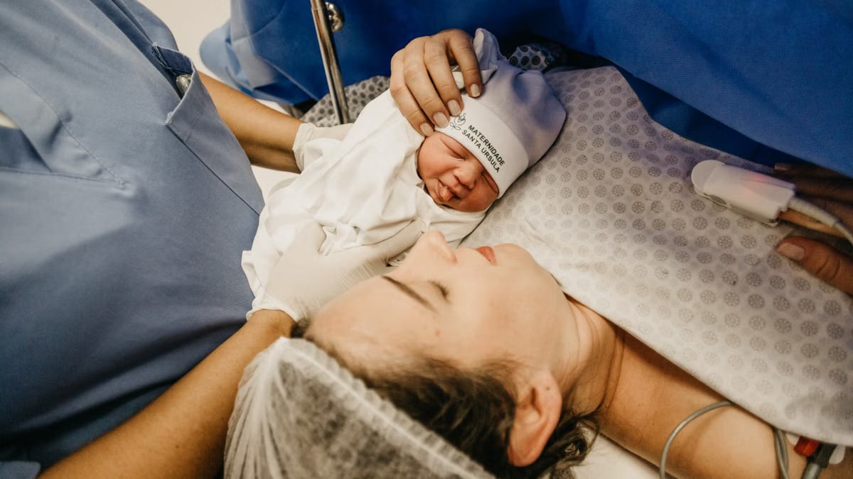 A mother cradling her newborn immediately after childbirth in a hospital setting.